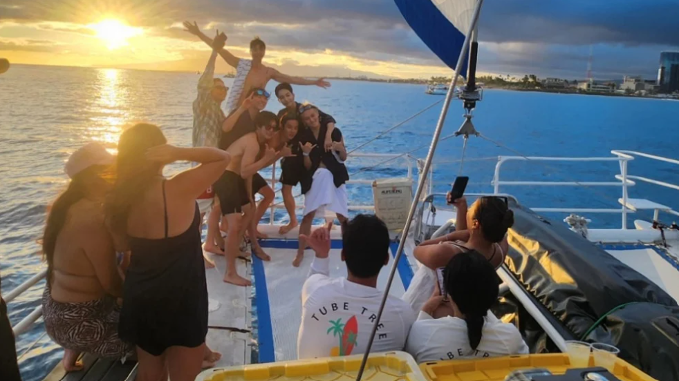 Group of friends enjoying a sunset on a private catamaran in Hawaii, posing for photos on deck with ocean views and a relaxed, celebratory atmosphere.